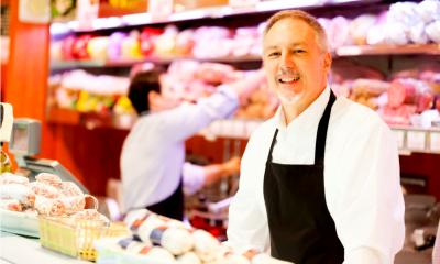 Two men in white overalls with a black apron on stood behind the counter at a delicatessen