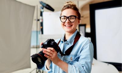 Una fotógrafa con gafas y una camisa azul que sostiene una cámara réflex digital