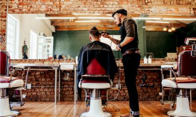 Customer sat in a chair getting his hair shaved by a barber in shop