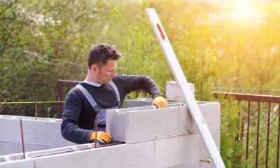 Builder using concrete blocks for building a wall at sunset