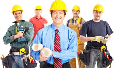 Construction manager holding building plans with four different tradesmen behind him