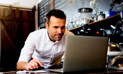 Cafe owner using his grey laptop to find out if he can franchise his business
