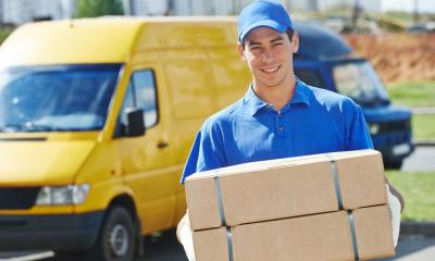 A blue uniformed courier delivering two large parcels from his yellow van