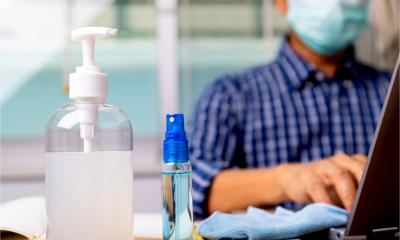 A male employee works at a desk containing a bottle of alcohol hand gel to prevent infection