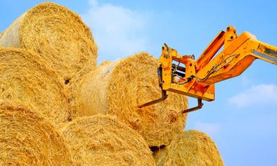 A yellow forklift moving hay bales on a sunny day