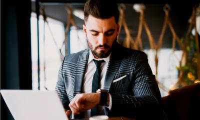 Bearded man in a suit looking at his watch while using his laptop