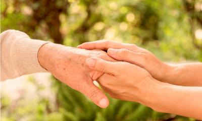 A person holding an older persons hand with blurred trees in the background