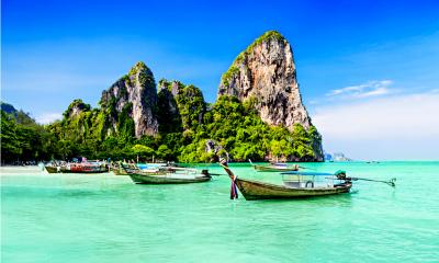 Multiple wooden boats in clear blue water with a large rock in the background on an exotic coastline