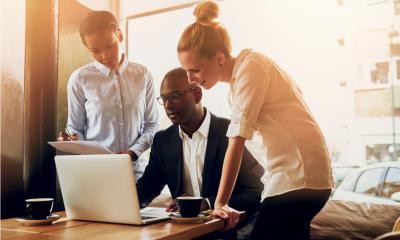Man sat down at a desk promoting his business to investors stood around him