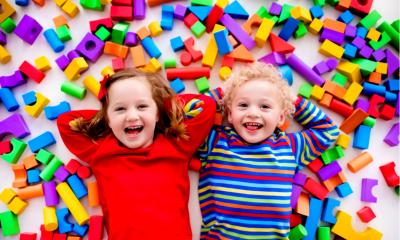 A boy and girl lying down with there hands behind their heads with toys around them