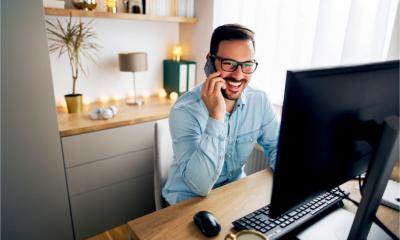 Smiling employee working remotely from home. He is speaking on the phone.