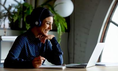 Smiling female manager in wireless earphones watches a training webinar on her laptop at home
