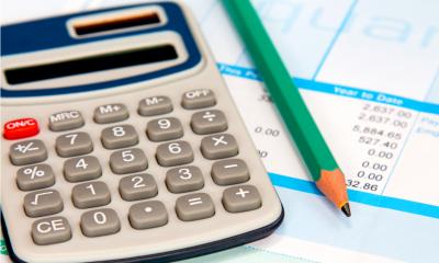 A calculator and pencil on a pay roll sheet calculating minimum wage