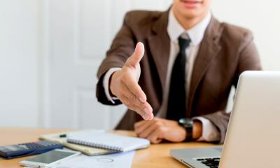 Businessmen in a brown suit offers handshake at his desk