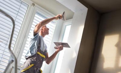 Plasterer working in living room next to the windows