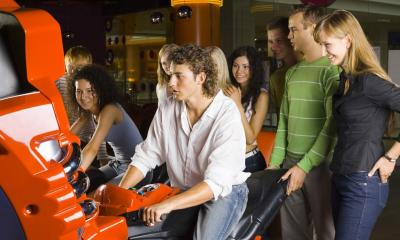 Group of friends at amusement arcade with two friends on motorbike game