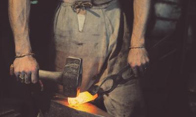 Blacksmith hammering hot metal in dark room