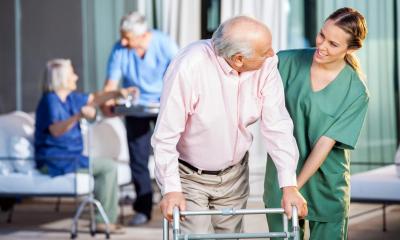 Carer helping old man walk with his frame with two people in background
