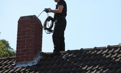 Man on roof sweeping a chimney on a sunny day
