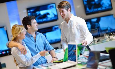 Man with arm around woman in computer shop being served by employee