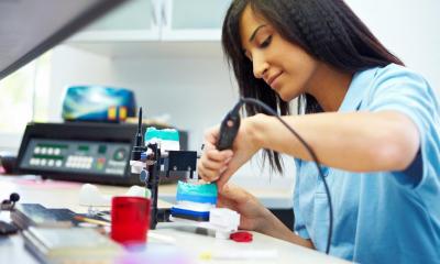 Woman with brown hair in blue scrubs using dental equipment