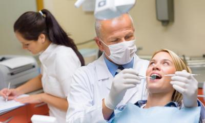 Male dentist treating a female patient with assistant in background