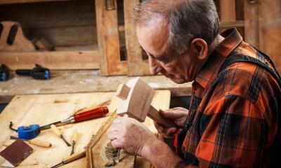 Old man using hammer and chisel on wooden furniture