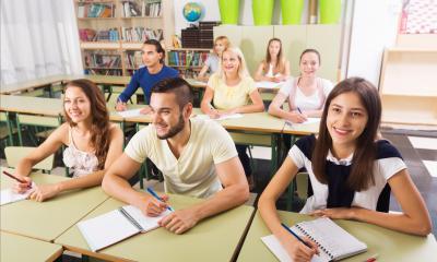 Multiple students in a classroom writing in their notepads