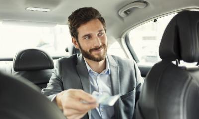 Man in back on minicab giving cash to driver