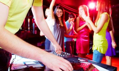 DJ using decks at party with people dancing in background