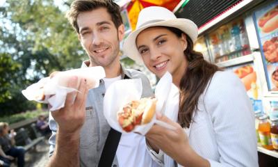 Man and woman eating hot dogs outside hotdog stand