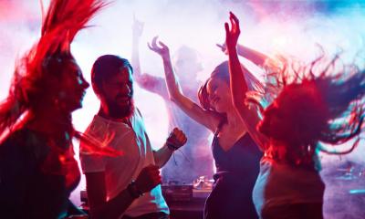 flere mennesker danser i mørk natklub med lys i baggrunden
