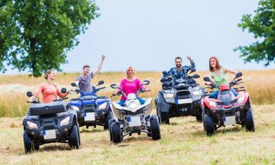 Multiple people riding quad bikes in open field on cloudy day