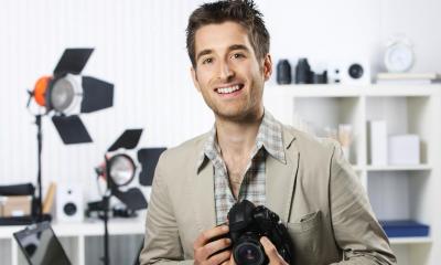 Man in beige suit holding black camera in photo studio