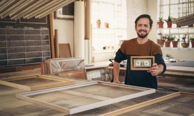 Man in jumper holding small framed picture in picture framing shop