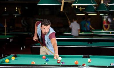 Man in waistcoat playing pool in dark room with peoples and tables in background