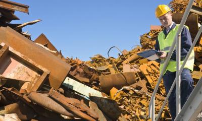 Man in high visibility vest in metal scrapyard with blue skies in background