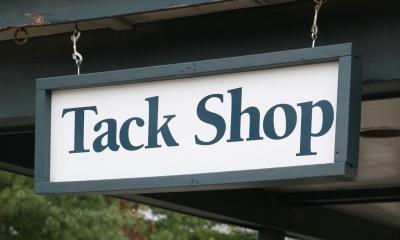 Green tack shop sign hanging down from wooden pillar
