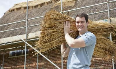 Man holding thatching materials with thatched house in background
