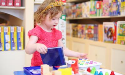 Little girl in pink top playing with different toys in toy shop