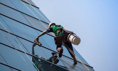 Person on the side of glass building cleaning windows with blue sky