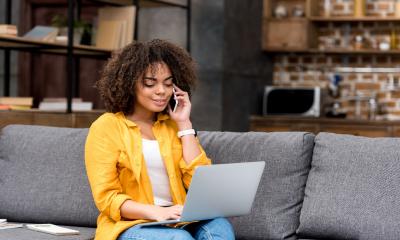 A young woman talks on the phone to a colleague whilst working on her laptop from home