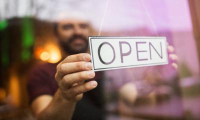 A small business owner turns the sign in the window as he opens his shop for the day