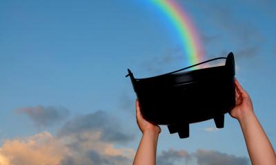Person holding up a black bucket to the sky with a rainbow in the background