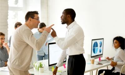 Two male colleagues have a disagreement in the office whilst others look on