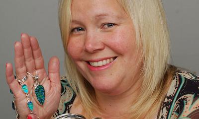 Female entrepreneur holding jewellery from her fingers while smiling at the camera
