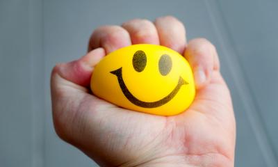 Person squeezing a yellow stress ball with a smiling face on it