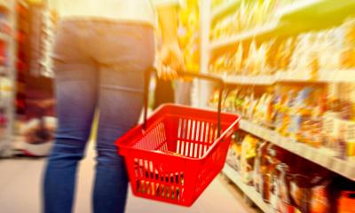 A shopper carries a red shopping basket in a shop aisle