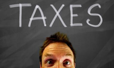 A man pops his head up below the work taxes on a blackboard