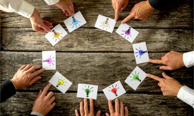 Businesspeople around a table each placing cards with lightbulbs drawn on them